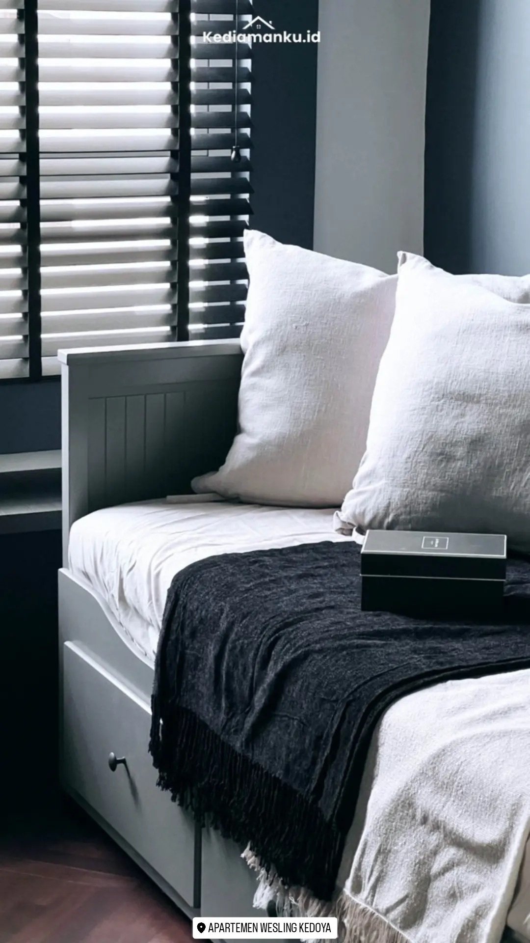 Sudut duduk Apartemen Wesling dengan bantal putih dan tirai horizontal
